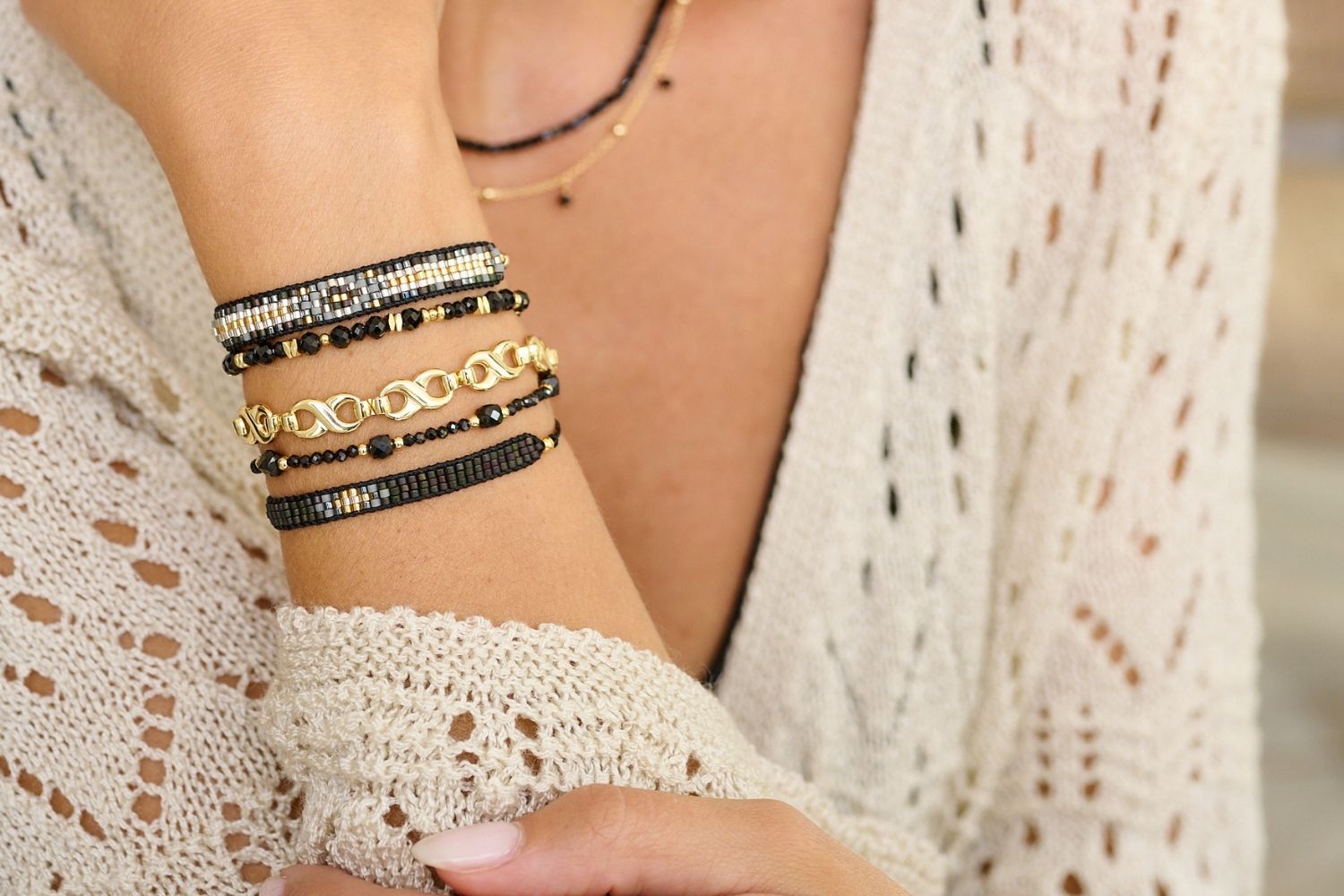 A stunning lifestyle picture showcasing the Bliss Black Spinel Gemstone Bracelet stacked amongst other black stacking bracelets and bracelets with gold accents